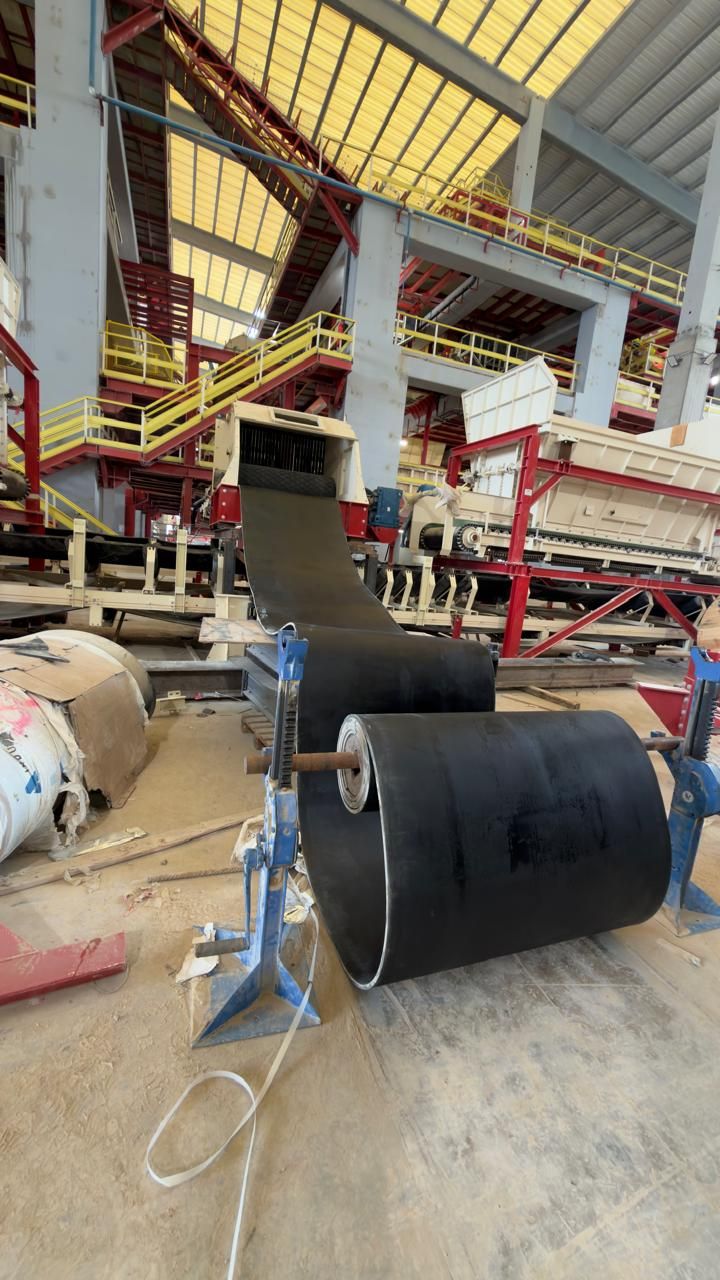 Deux rouleaux de bande transporteuse neuve sur supports métalliques au sol d'un atelier industriel, structure de criblage à l'arrière-plan