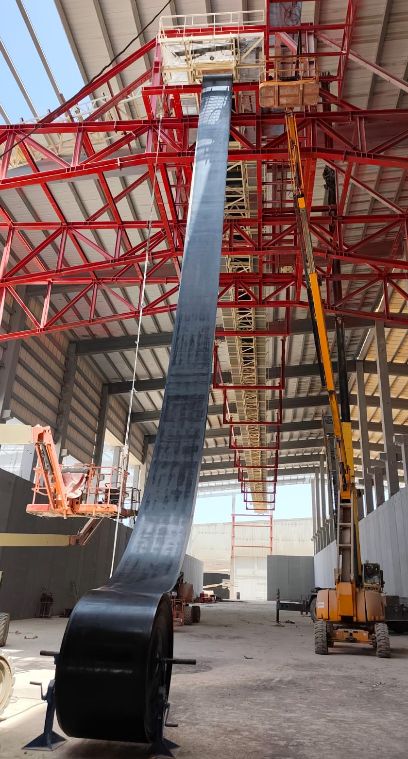 Longue bande transporteuse montant à la verticale dans une structure métallique rouge