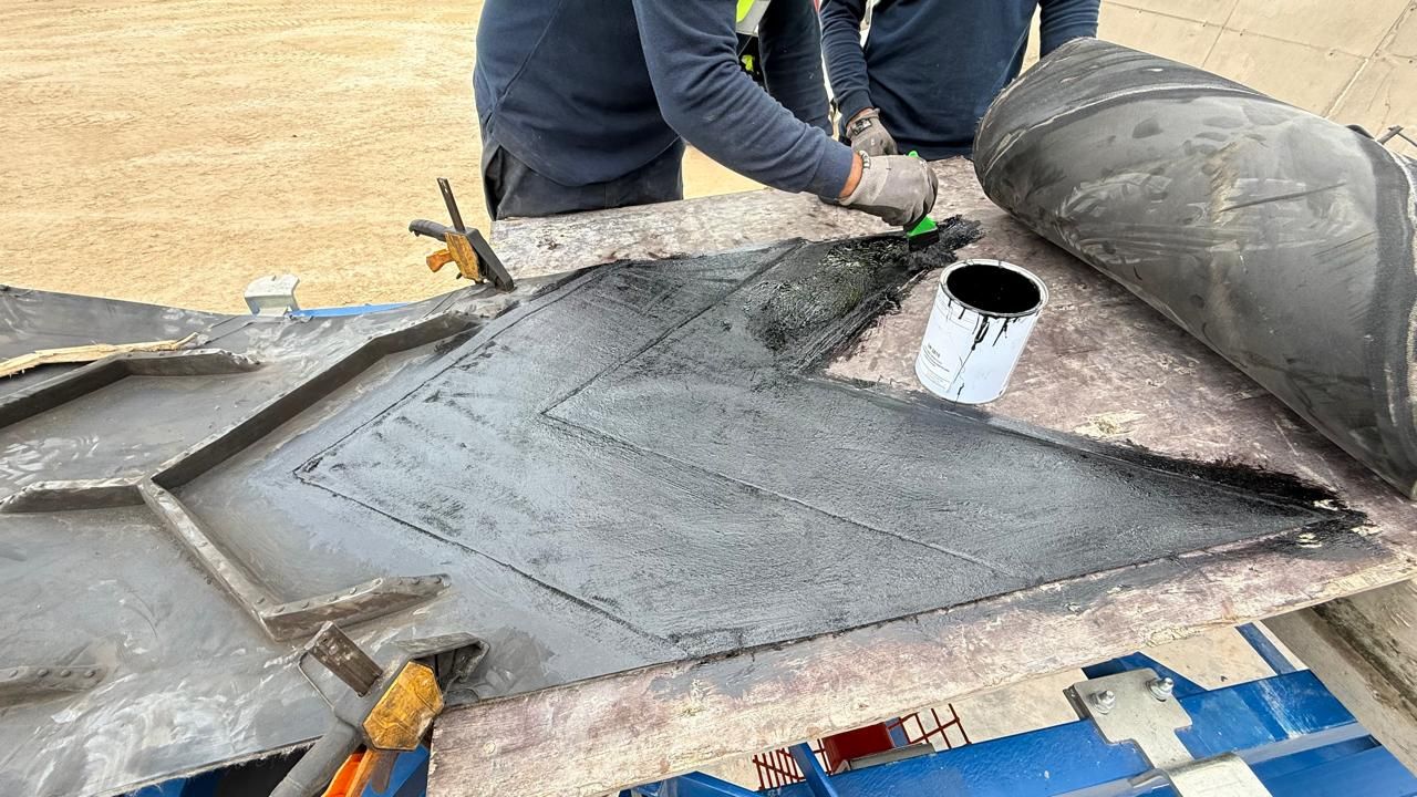 Mains gantées appliquant de la colle au pinceau sur une pièce de réparation en caoutchouc découpée, pot de colle ouvert, bande roulée à proximité