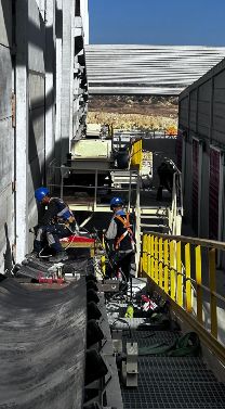 Deux techniciens sur une passerelle surélevée le long d'un grand convoyeur