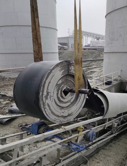 Grand rouleau de bande sur un support de déroulage près de silos